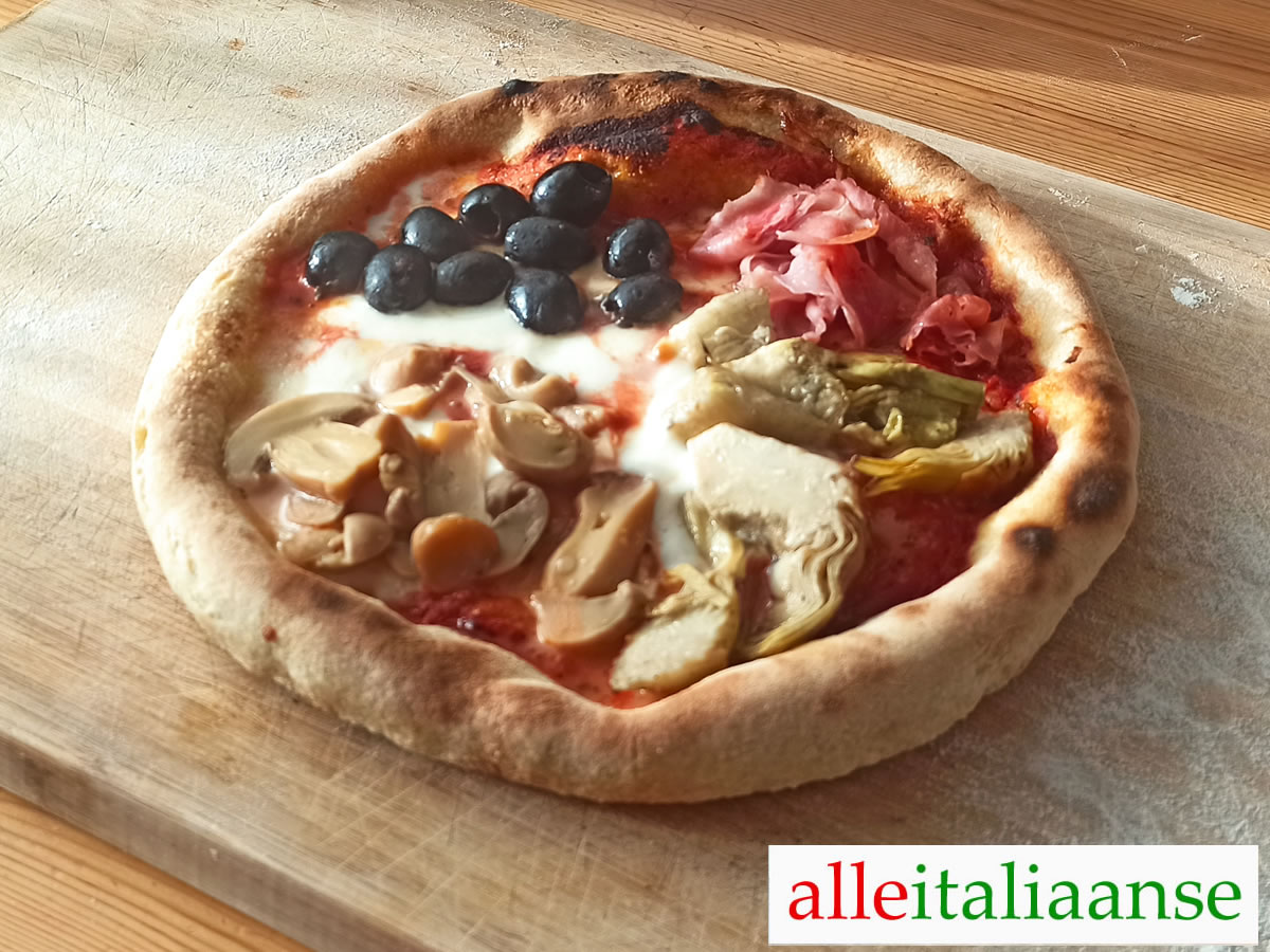 Een zelfgemaakte pizza Quattro Stagioni met tomaat, mozzarella, zwarte olijven, artisjokken, ham en champignons